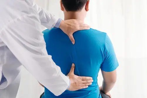 A chiropractor helps a patient with back discomfort by offering a spinal adjustment.
